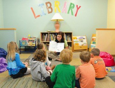 children sitting on the floor reading books in front of a library sign that reads library