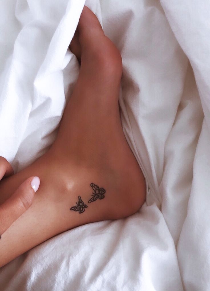 a person laying on top of a bed covered in white sheets with tattoos on their legs