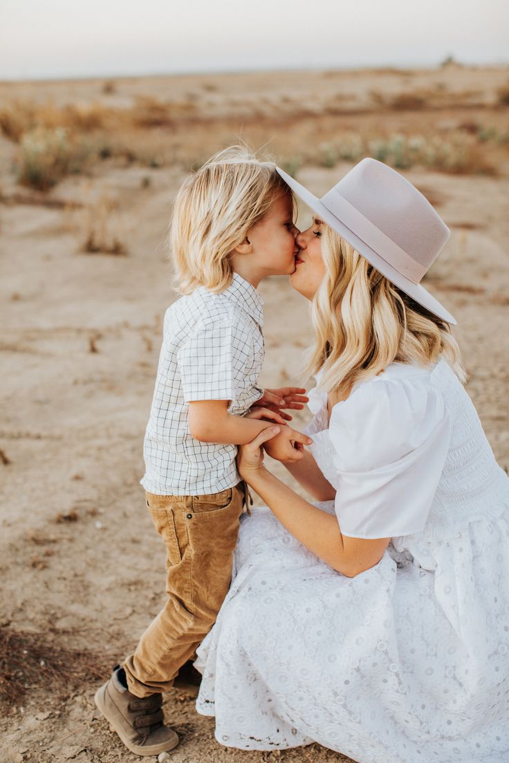 a mother kissing her son on the cheek while he is wearing a cowboy hat and white dress