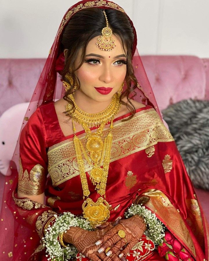 a woman in a red and gold bridal outfit sitting on a pink couch with her hands together