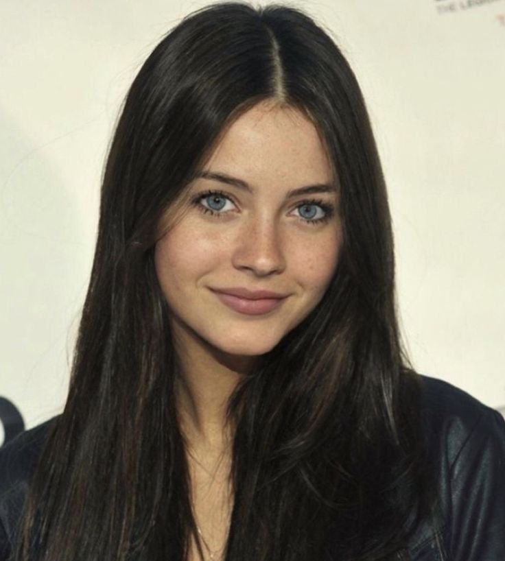 a woman with long brown hair and blue eyes smiles at the camera while wearing a black leather jacket