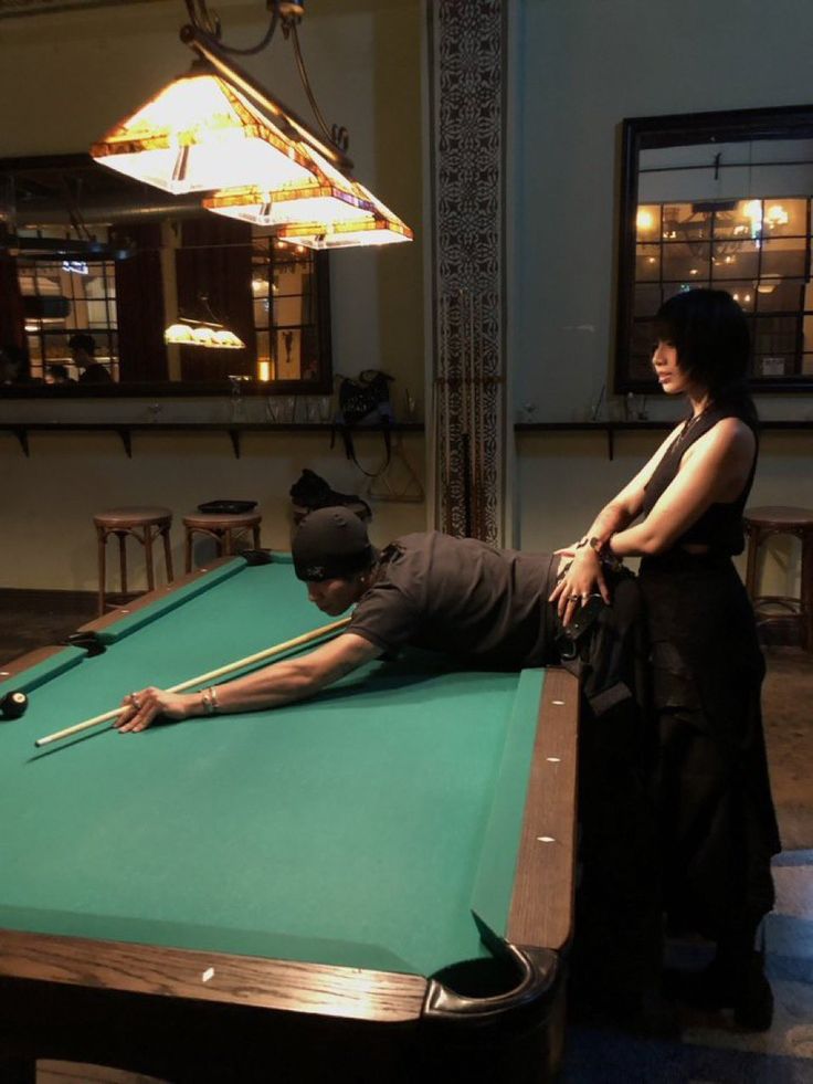 a man and woman playing pool in a large room with lights hanging from the ceiling