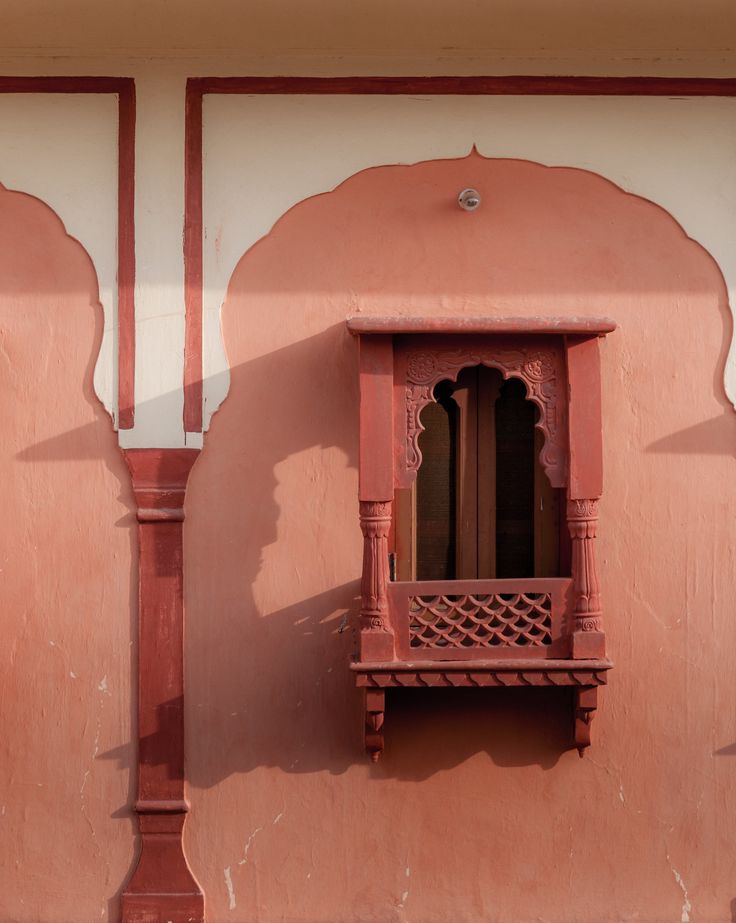 an ornate window with wooden balconies on the side of a pink stucco building