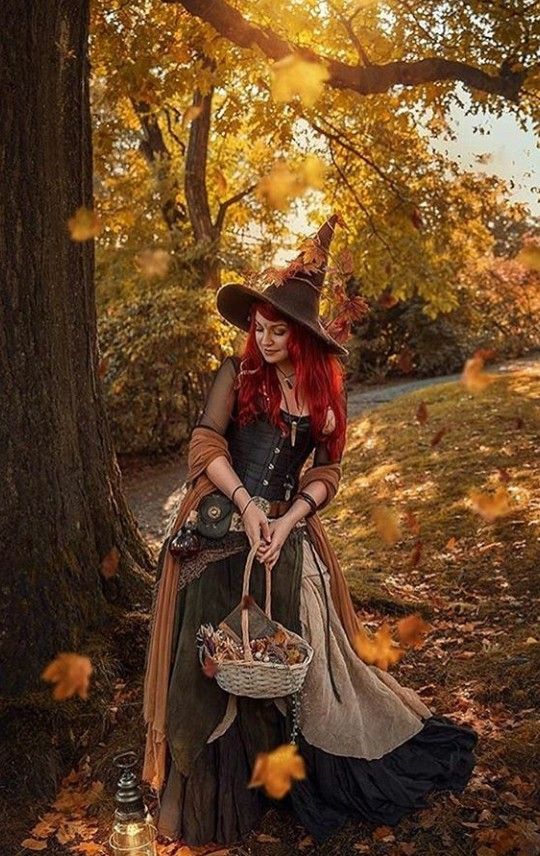 a woman dressed as a witch sitting under a tree with a basket in her hand