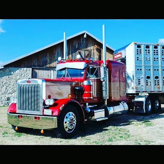 a red and silver semi truck parked in front of a barn