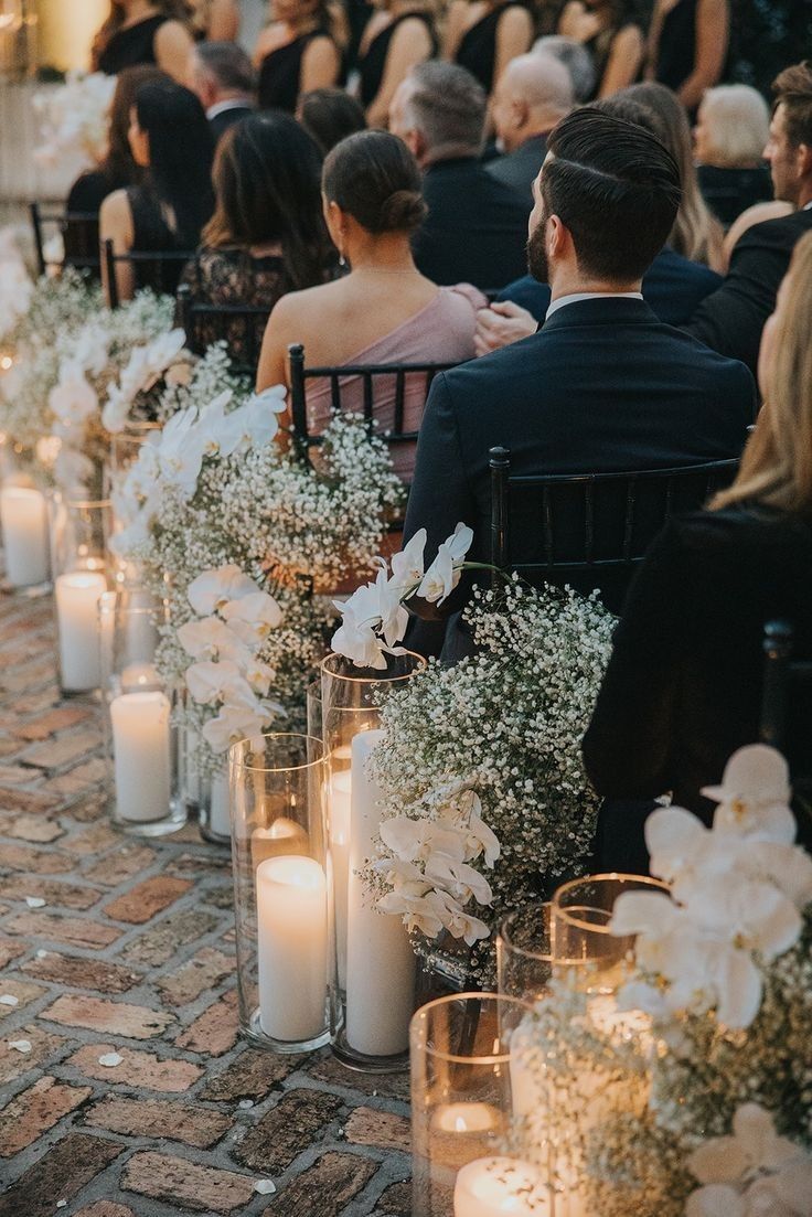 a row of chairs with flowers and candles on them in front of people sitting down