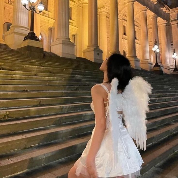 a woman in a white dress is walking up some steps with an angel wings on her back