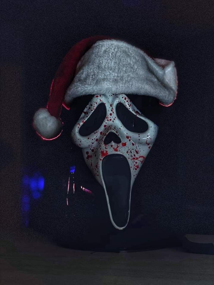 a creepy mask wearing a santa hat with blood splattered on it's face