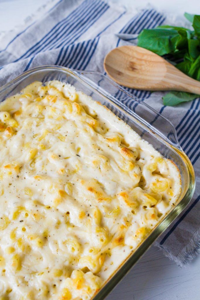 a casserole dish with cheese and spinach on the side next to a wooden spoon