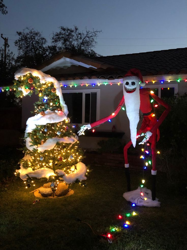 two christmas decorations in front of a house with lights on the trees and one decorated to look like santa clause