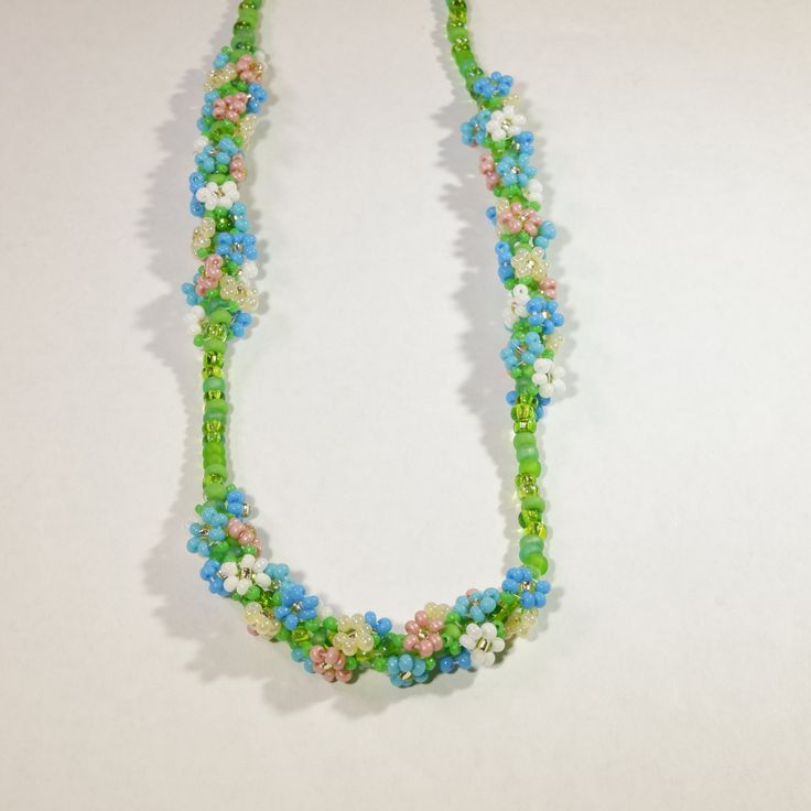 This dainty springtime necklace features three bundles of beaded daisies, woven in a spiral around multicolored green glass beads. The daisies come in shades of pink, blue, white, and cream, each with its own set of tiny leaves. This necklace looks beautiful at a variety of lengths, but was designed to be a choker (14-16in) or princess (18in) necklace. This necklace is made-to-order. Please allow 3-5 business days for processing. Spring Beaded Flower Necklace, Beaded Flower Necklace For Spring, Spring Flower Necklace With Colorful Round Beads, Handmade Flower Beaded Necklace For Spring, Spring Flower Necklace With Round Beads, Spring Beaded Flower Necklace With Round Beads, Spring Tiny Round Beaded Necklaces, Handmade Blue Necklaces For Spring, Spring Gift Beaded Necklaces With Tiny Beads