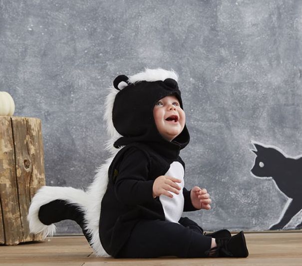 a small child in a costume sitting on the floor next to a wall with a black and white cat painted on it