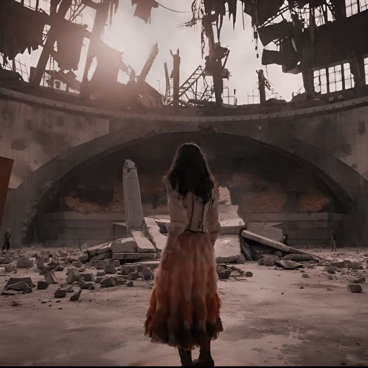 a woman standing in an abandoned building looking at the ground with debris all around her