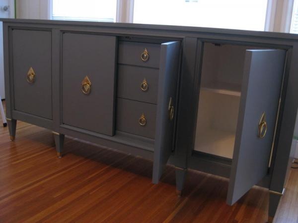 a large gray cabinet with gold handles in a room next to a window and hardwood floor