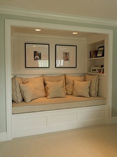 a window seat with pillows and pictures on the wall above it in a living room