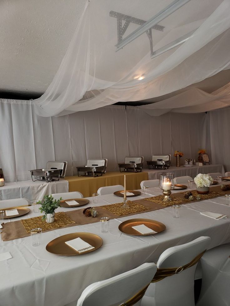 a long table with white linens and gold place settings is set up for an event