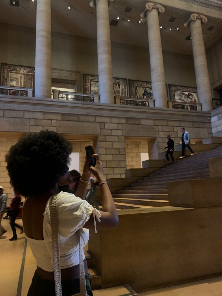 a woman taking a photo with her cell phone at the top of stairs in a building