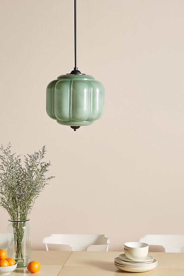 a green light hanging over a dining room table with plates and oranges on it