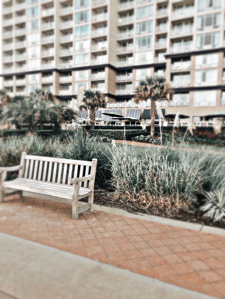 a white bench sitting on top of a brick walkway next to tall buildings and palm trees