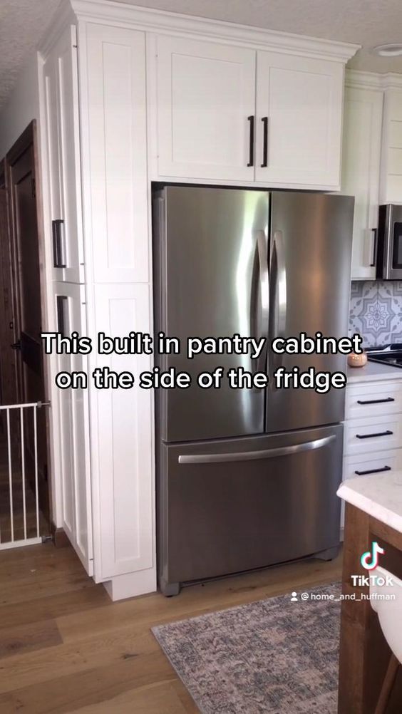 a stainless steel refrigerator in a kitchen with white cabinets and wood flooring that says, this built in pantry cabinet on the side of the fridge