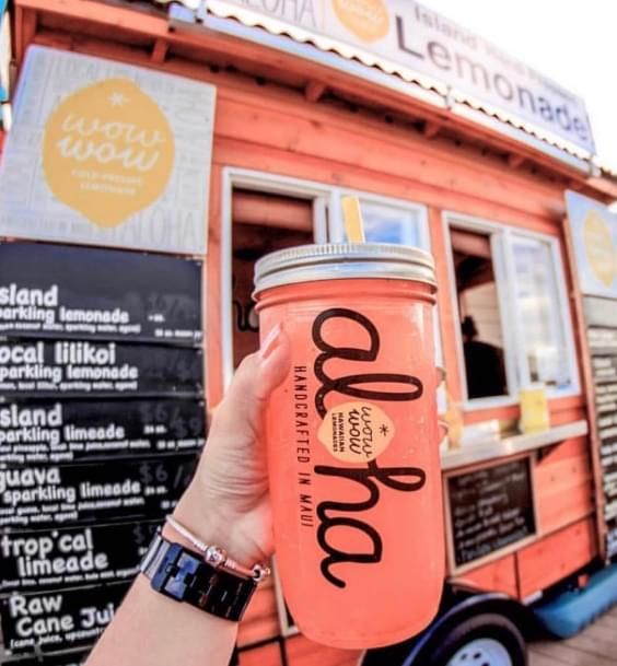 a person holding up a pink drink in front of a food truck