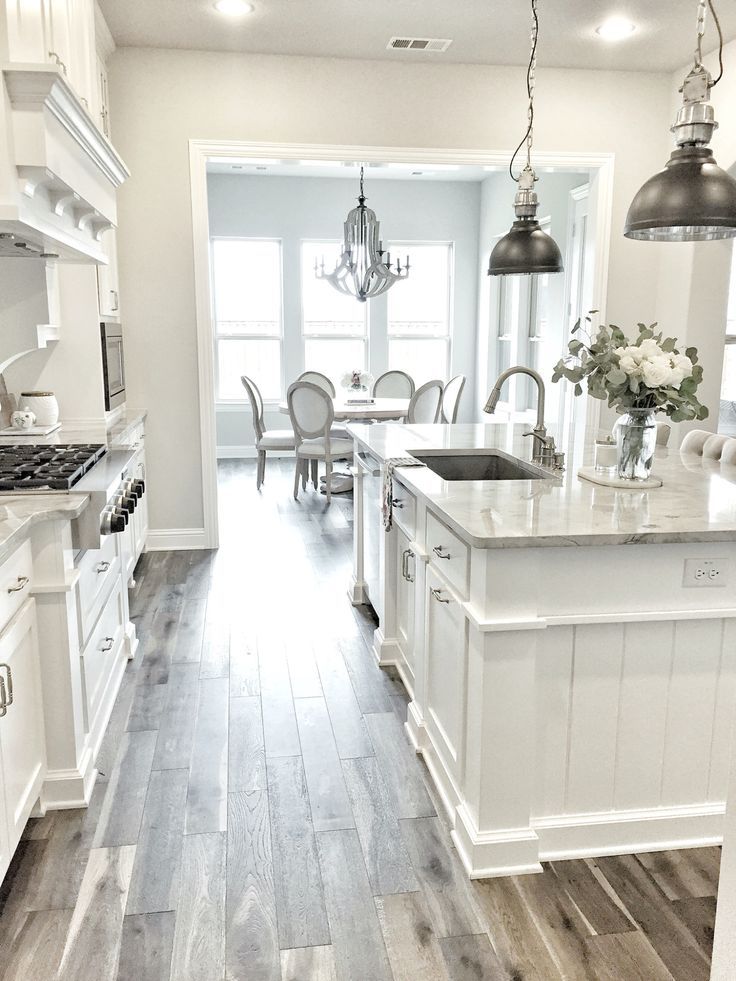 a large kitchen with white cabinets and wood flooring is seen in this image from the front door