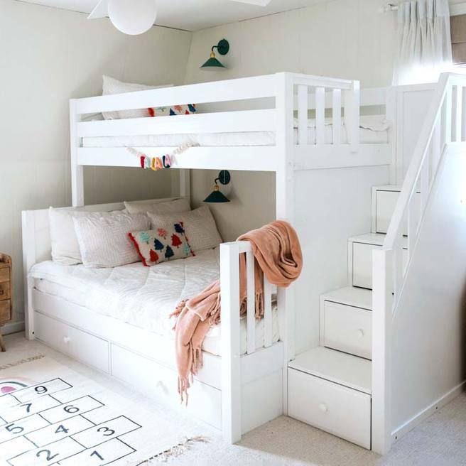 a white bunk bed sitting next to a stair case in a room with carpeted flooring