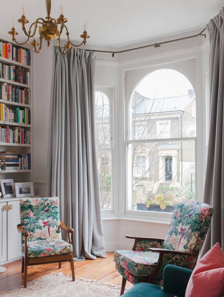 a living room filled with furniture and a chandelier hanging from the ceiling next to two windows