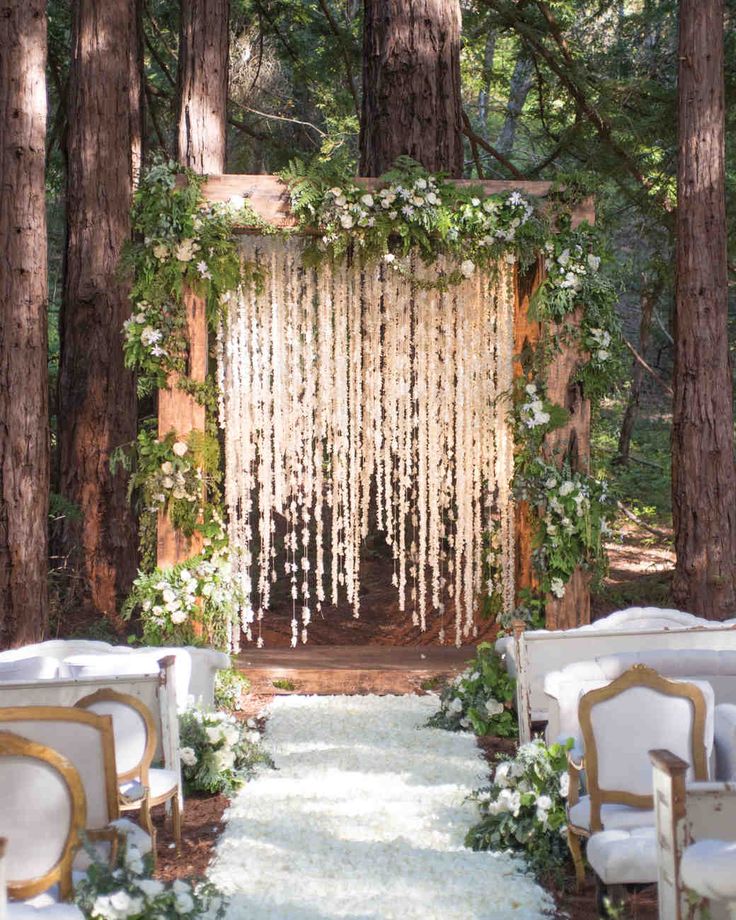 an outdoor ceremony in the woods with white flowers and greenery hanging from the trees