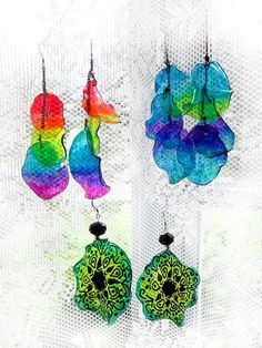 three colorful earrings hanging from hooks on a white background with the colors of the rainbow