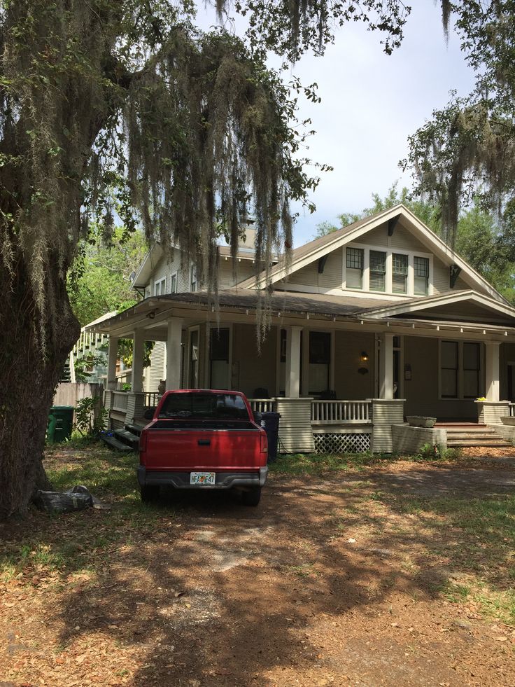 a red truck is parked in front of a house with spanish moss on the trees