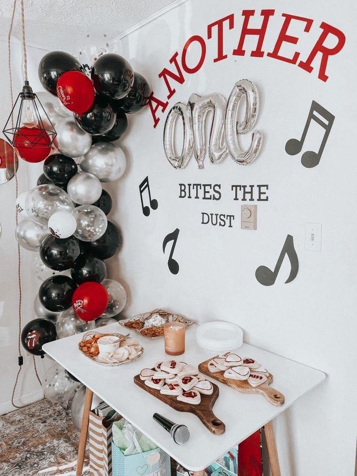 a table topped with lots of desserts next to a wall covered in balloons and music notes