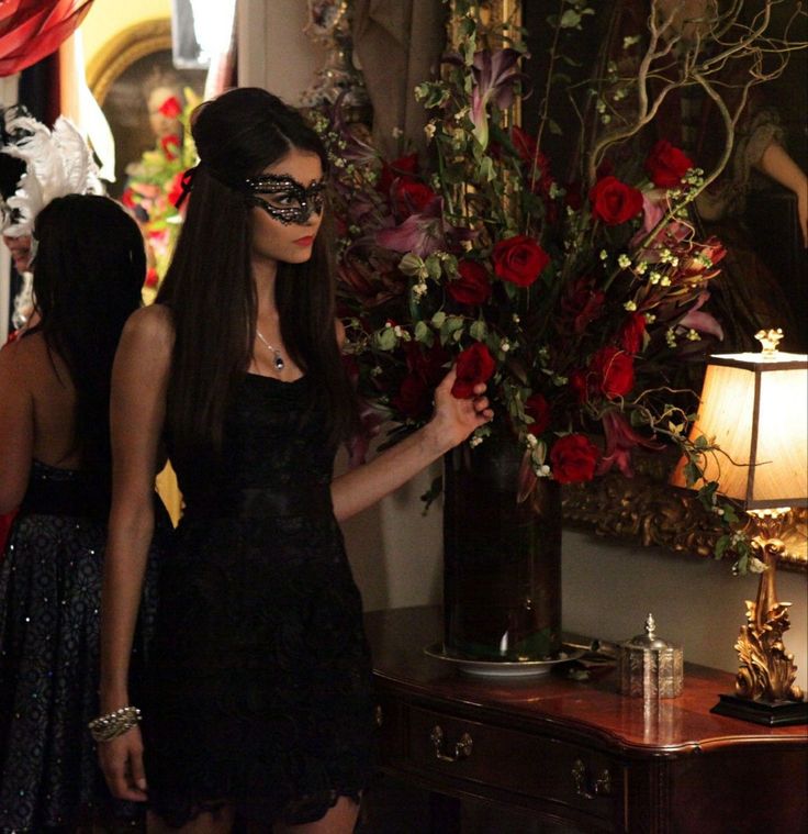 a woman in a black dress standing next to a table with flowers and candles on it