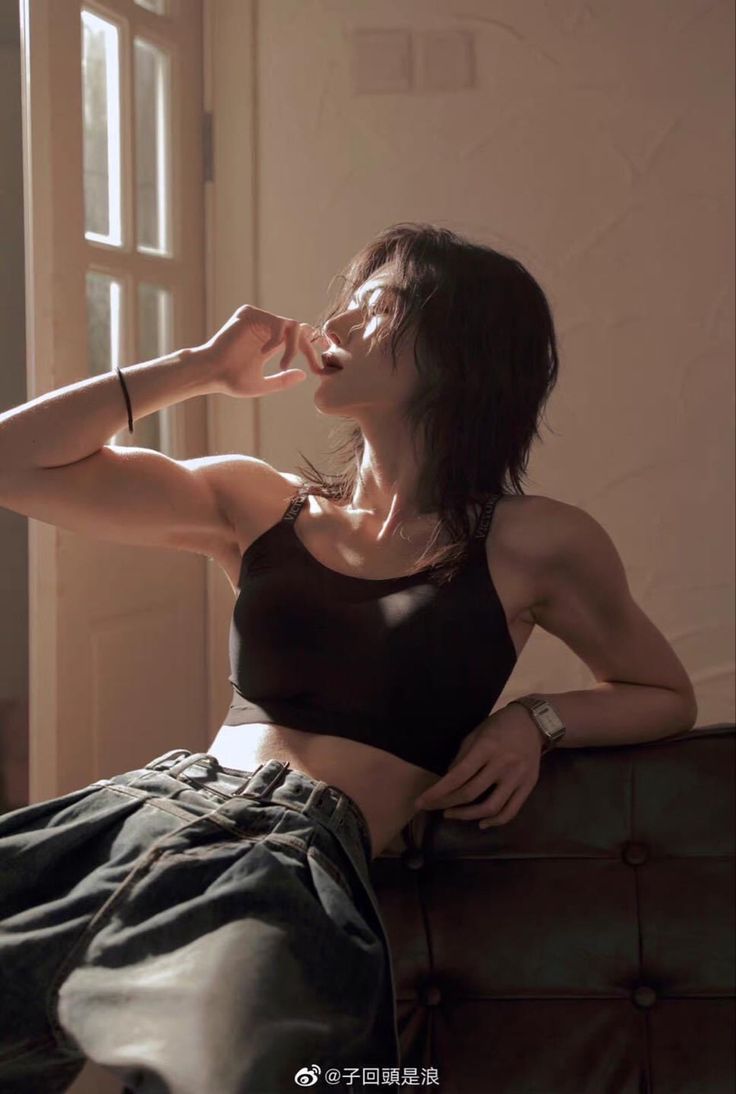 a woman sitting on top of a couch in a black bra and khaki pants