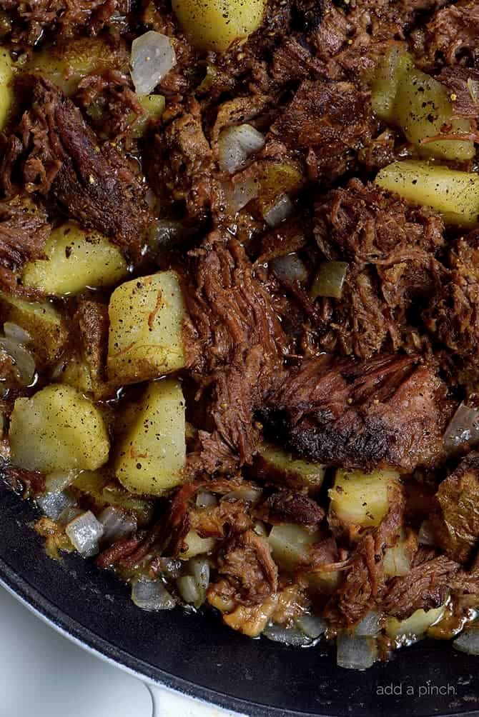 cooked meat and potatoes in a skillet on a stove top with seasoning sprinkles