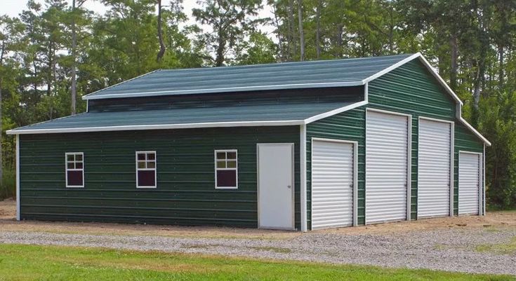 a green garage with white trim and two doors on the side, in front of some trees