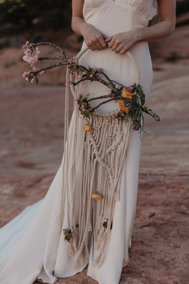 a woman wearing a white dress holding a flower and beaded dream catcher in her hand