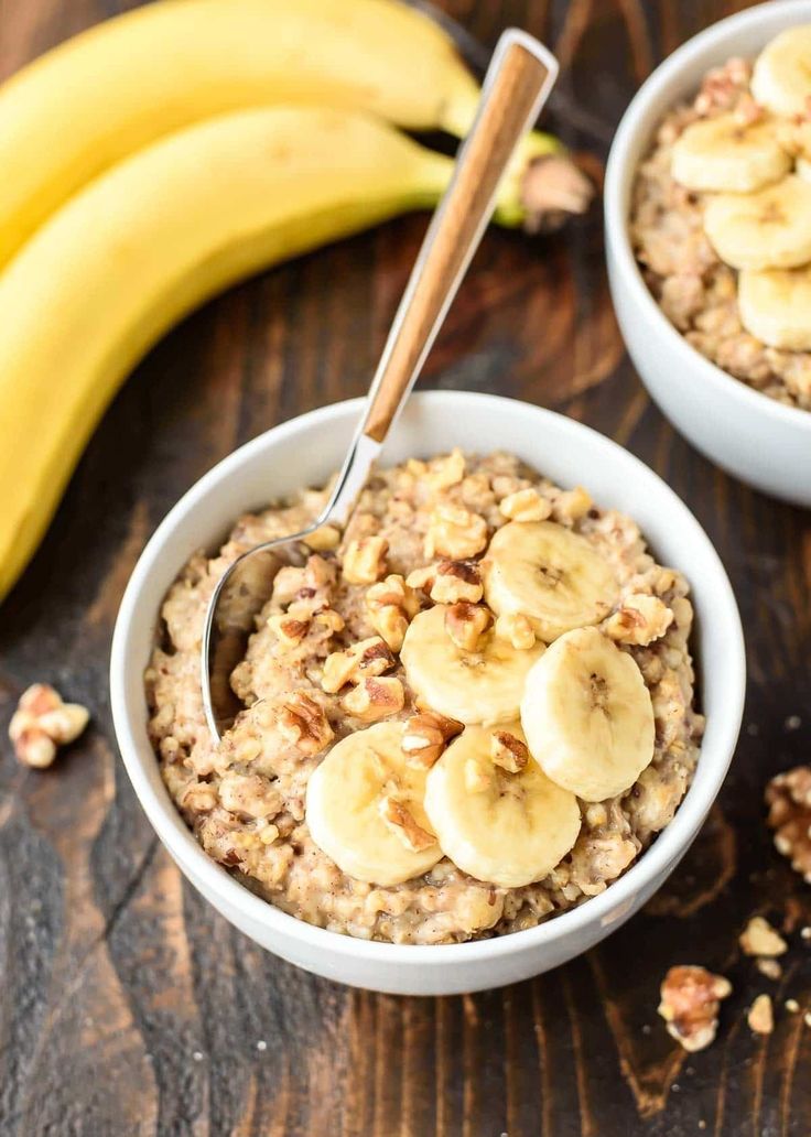 two bowls of oatmeal with bananas and walnuts on a wooden table