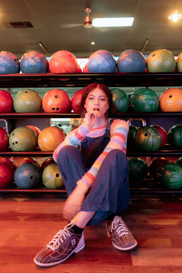 a woman sitting on the floor in front of bowling balls