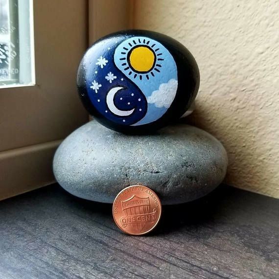 a coin sitting on top of a rock next to a window sill with the sun and moon painted on it