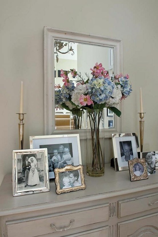 a mantle with flowers, pictures and candles on it in front of a large mirror