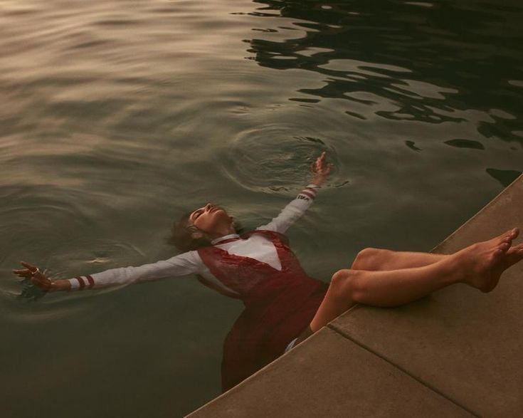 a woman floating on top of a body of water next to a pier with her arms outstretched