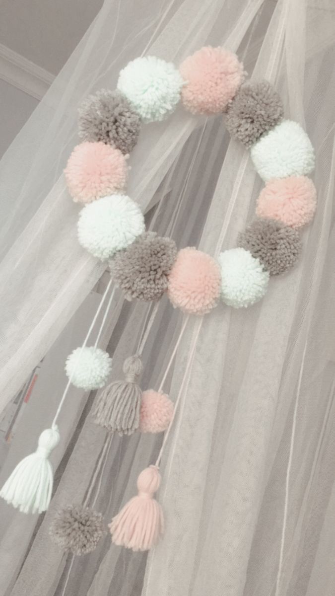 a pink and grey pom - pom garland hanging from a sheer curtain