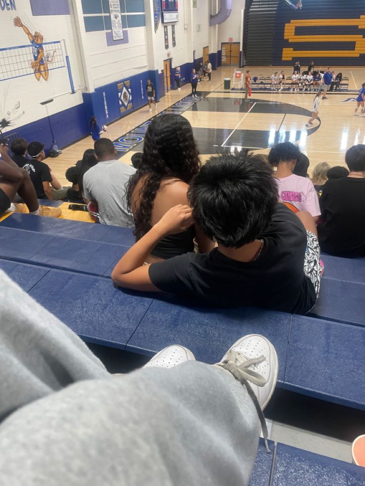 several people sitting on benches in a gymnasium watching basketball game with one person covering his face