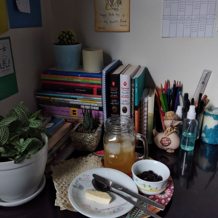 a table topped with books and cups filled with liquid next to a potted plant