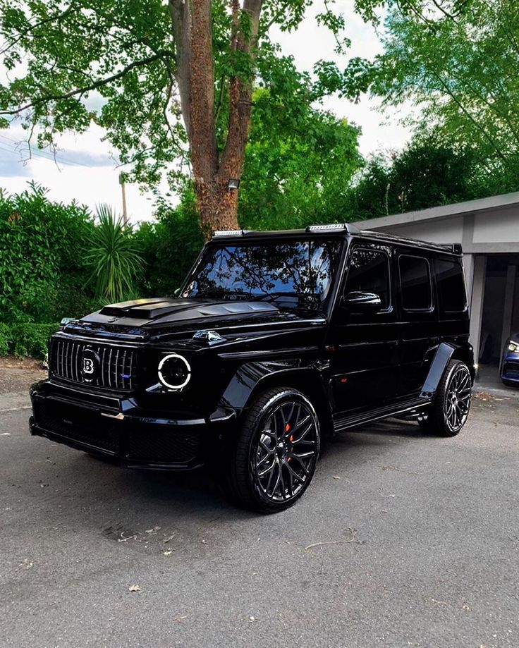 a black mercedes g - class is parked in front of a garage with its doors open