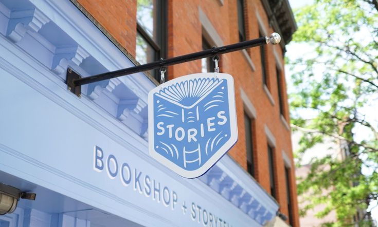 a store sign hanging from the side of a brick building with trees in the background