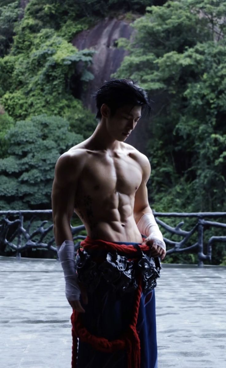 a man with no shirt standing in front of a waterfall and holding his hands on his hips