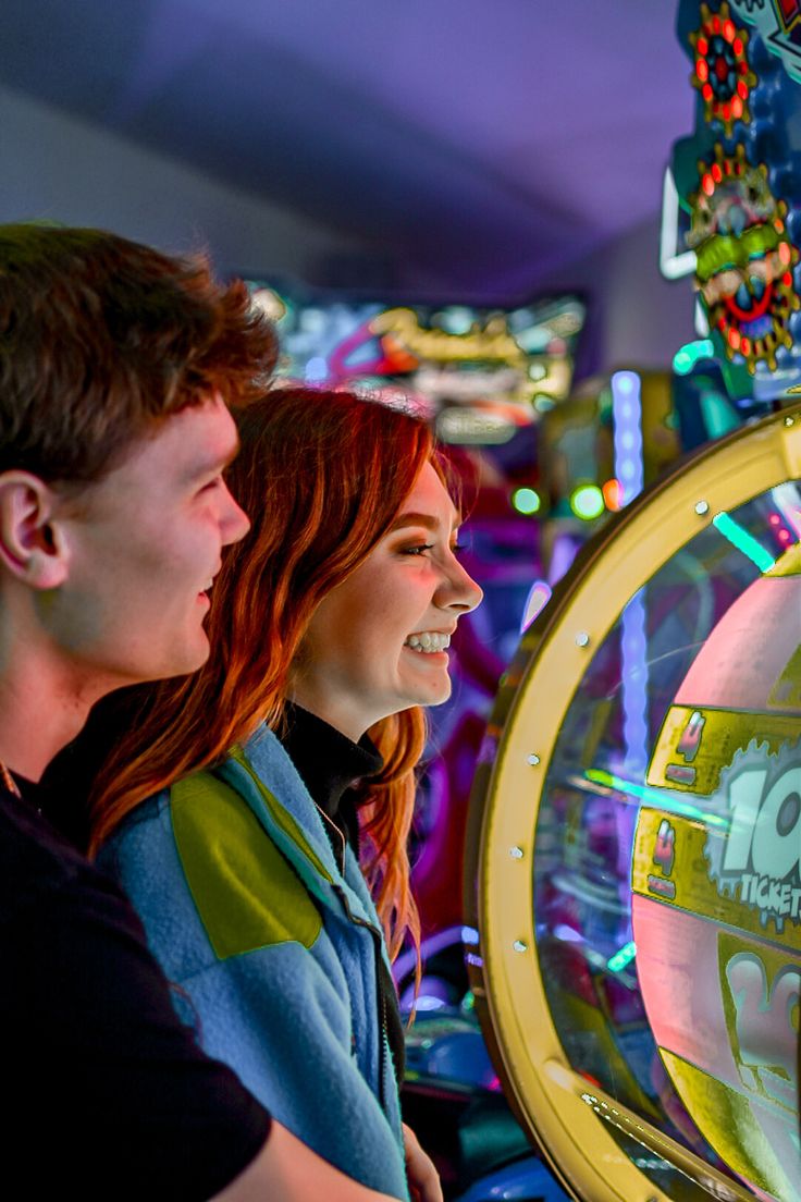 two people standing next to each other in front of a video game machine at night