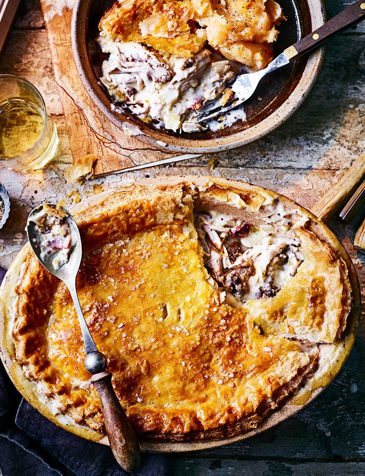 two pies sitting on top of a wooden table next to wine glasses and utensils